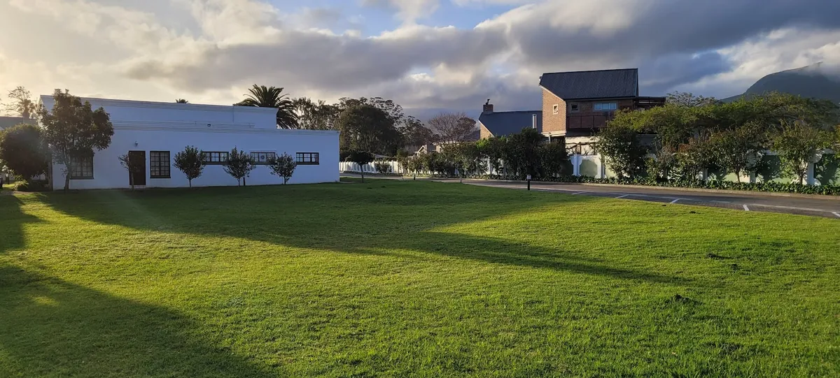 Low white Cape-Dutch style building on a manicured lawn at Fancourt, Outeniqua mountains looming behind under early-morning cloud