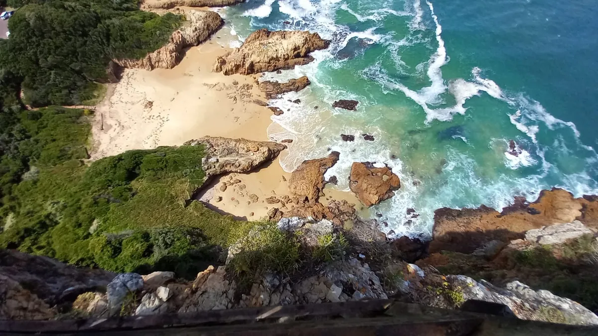 Top-down into Coney Glen from the Eastern Head viewpoint — wooden rail, sandy cove, surging tidal rocks