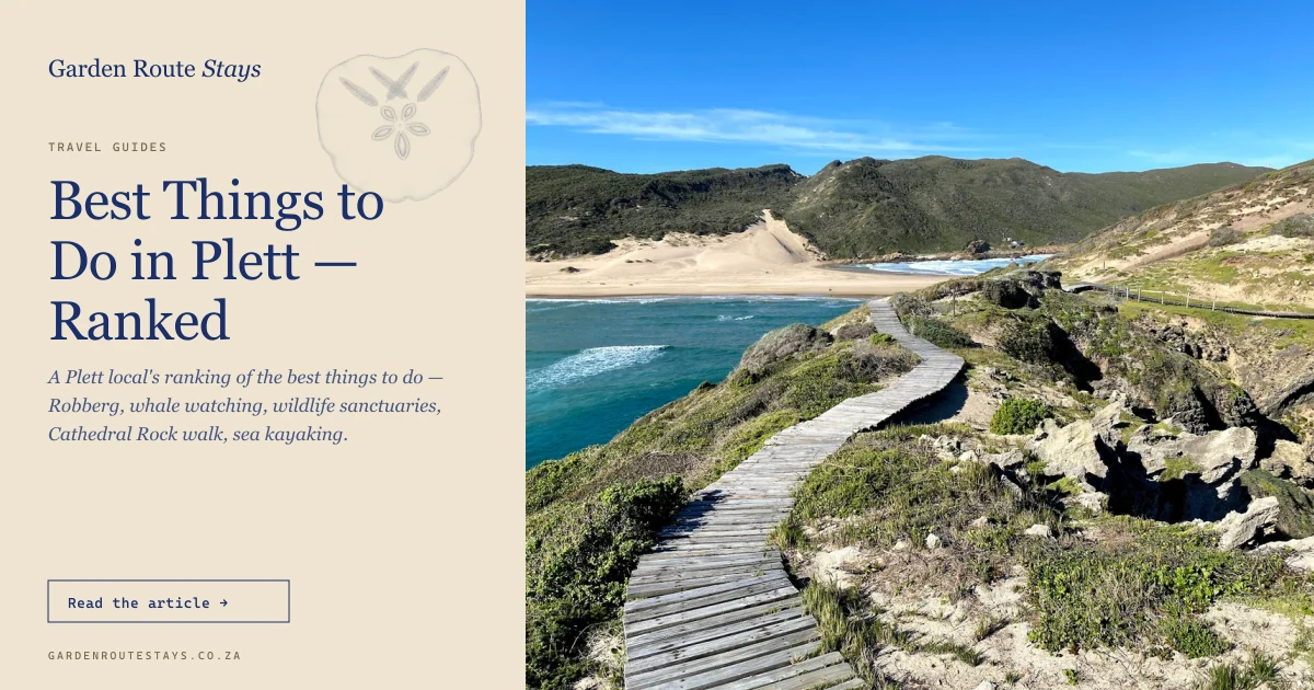 Robberg Nature Reserve boardwalk above the turquoise bay at Plettenberg Bay — timber walkway curving along the cliff, the peninsula and sandy isthmus in the distance