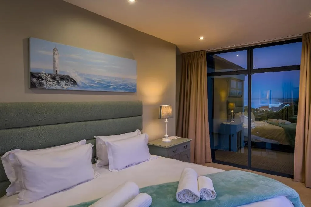 Modern bedroom with green headboard, white bedding, and panoramic sea view doors
