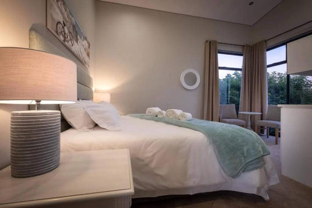 Modern bedroom with queen bed, fresh white linens, and garden views through windows