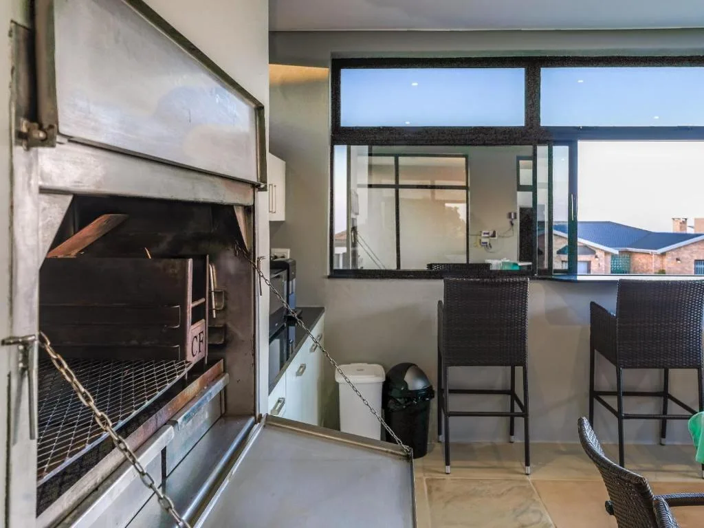 Outdoor braai area with built-in grill and high-top seating chairs overlooking town