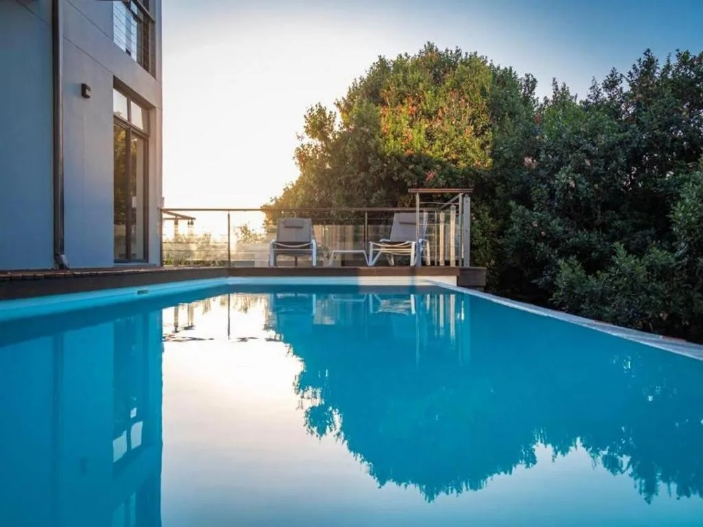 Sparkling blue swimming pool with modern white building and leafy trees