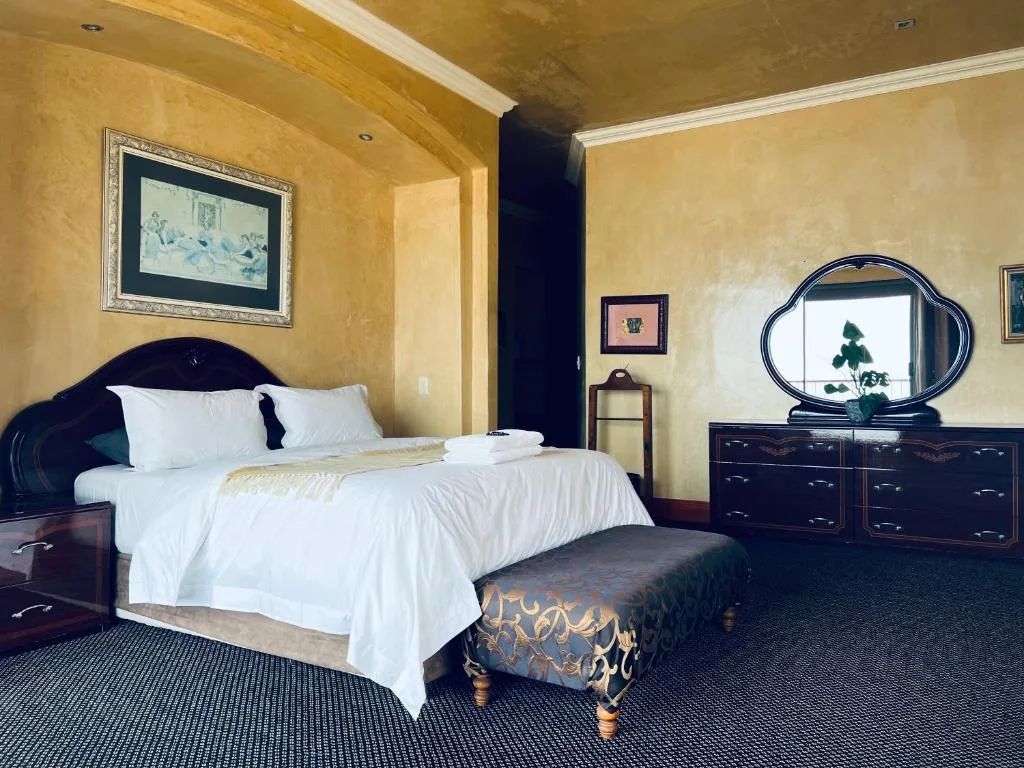 Elegant bedroom with white linens, dark wooden furniture, and golden walls