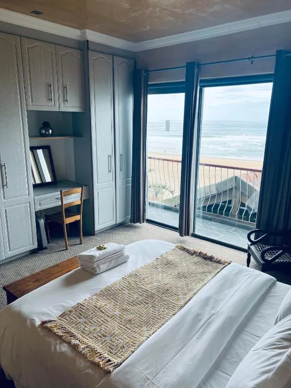 Beachfront bedroom with ocean view through glass doors and balcony