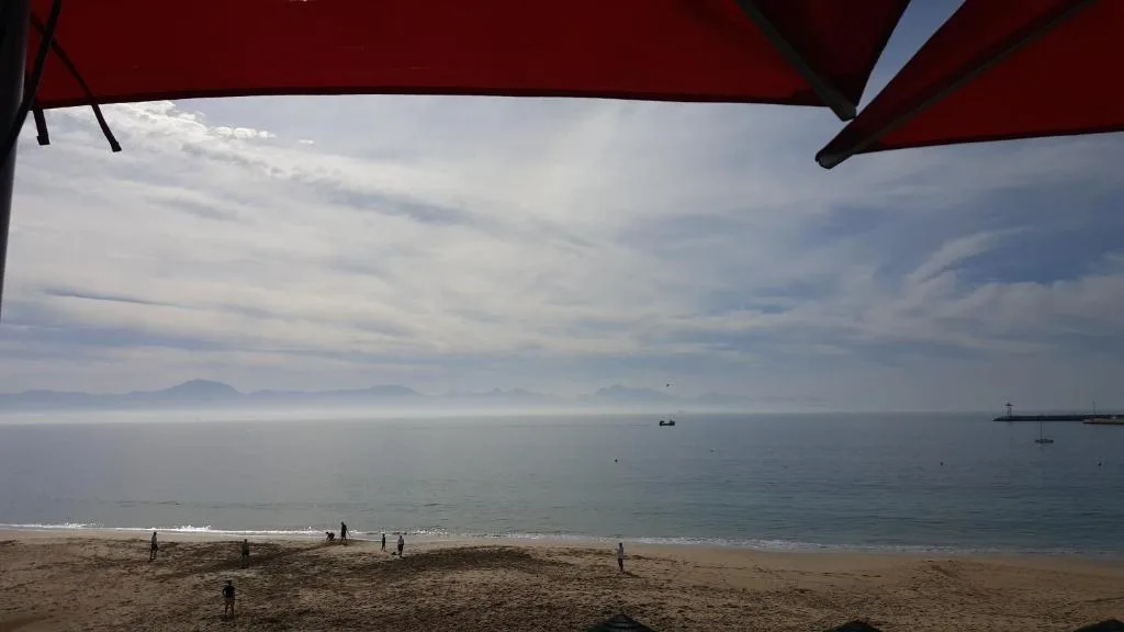 Tranquil beachfront vista with mountains, calm waters, and sandy shore