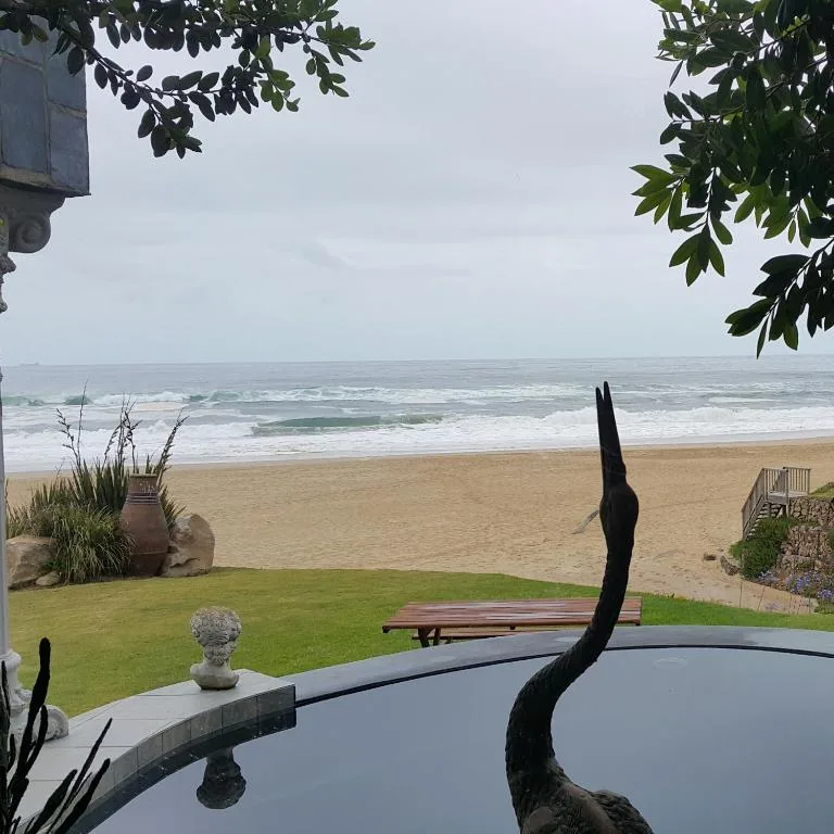 Beachfront vista with ocean waves, sandy beach, and green lawn from property