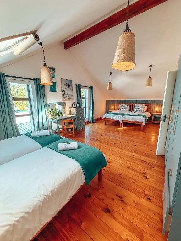 Spacious bedroom with two beds, wooden floors, pendant lighting, and turquoise curtains