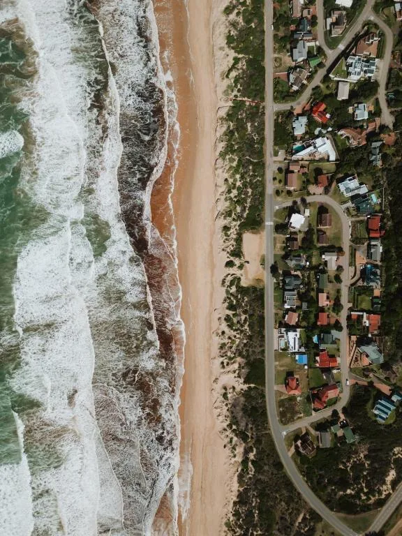 Aerial view of sandy beach, ocean waves, and beachfront residential properties