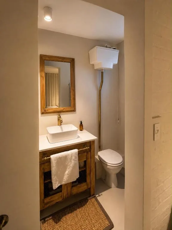 Compact bathroom with wooden vanity, white vessel sink, and toilet