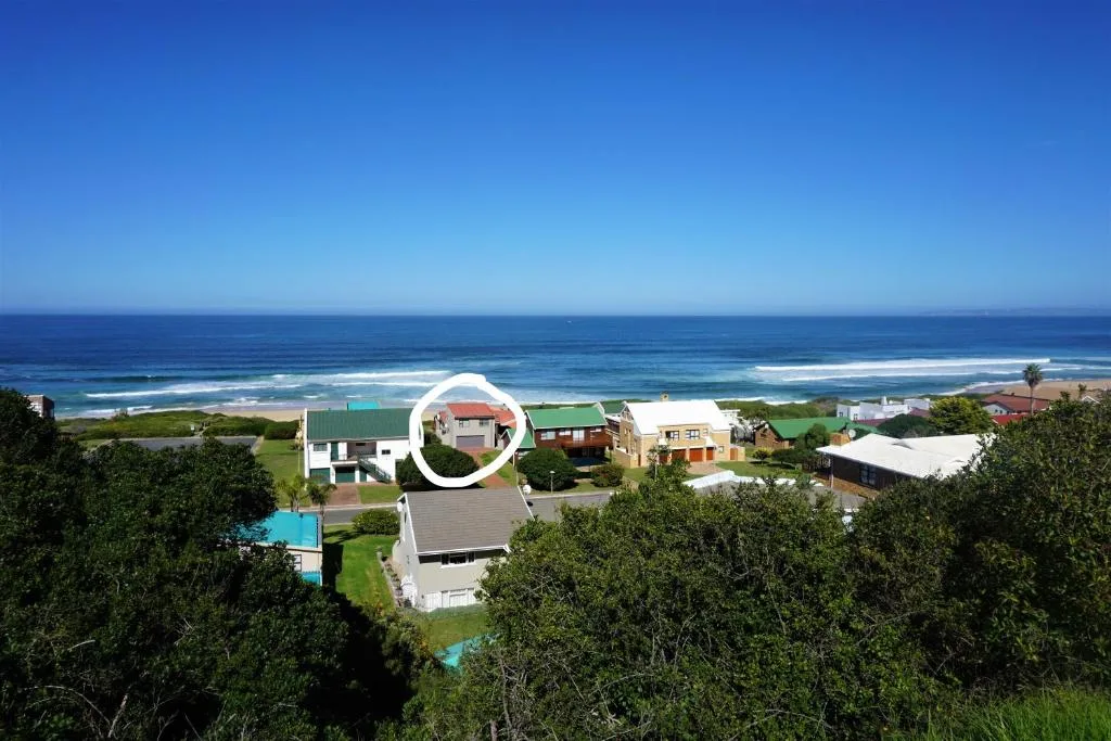 Coastal property with ocean, beach, and neighboring homes visible from elevated vantage point