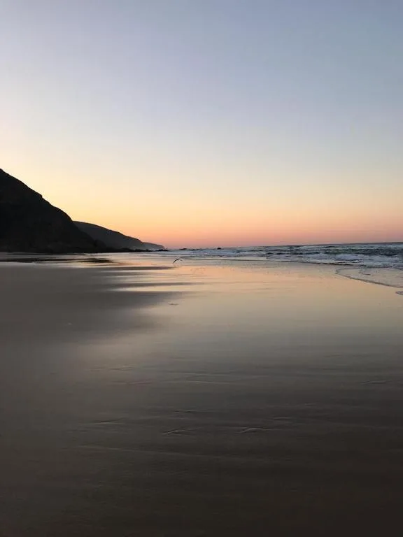 Serene beach sunset with mountains and calm ocean waters at dusk