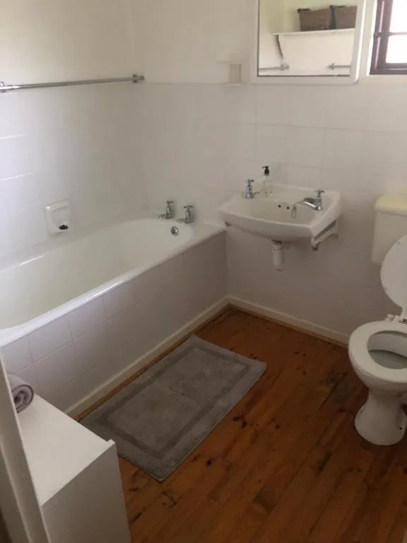 Clean bathroom with bathtub, sink, toilet, and wooden flooring