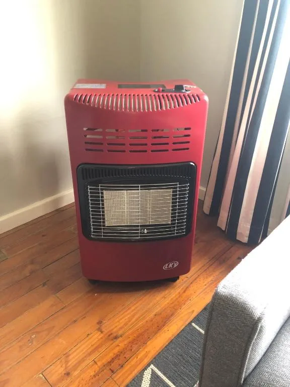 Red portable gas heater with safety grill on wooden floor
