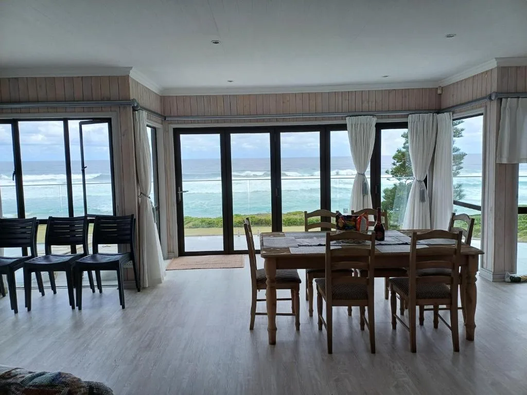 Dining table with wooden chairs overlooking ocean views through glass doors