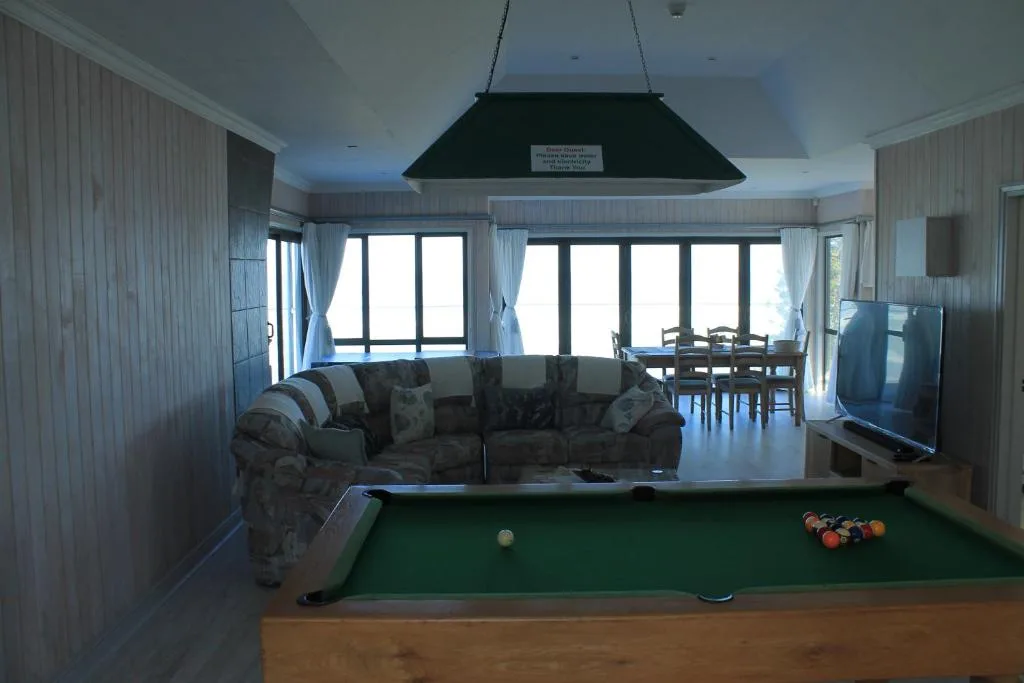 Open-plan lounge with pool table, sofa, and ocean views through large windows