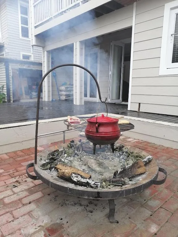 Red potjie pot over fire pit on brick patio near house