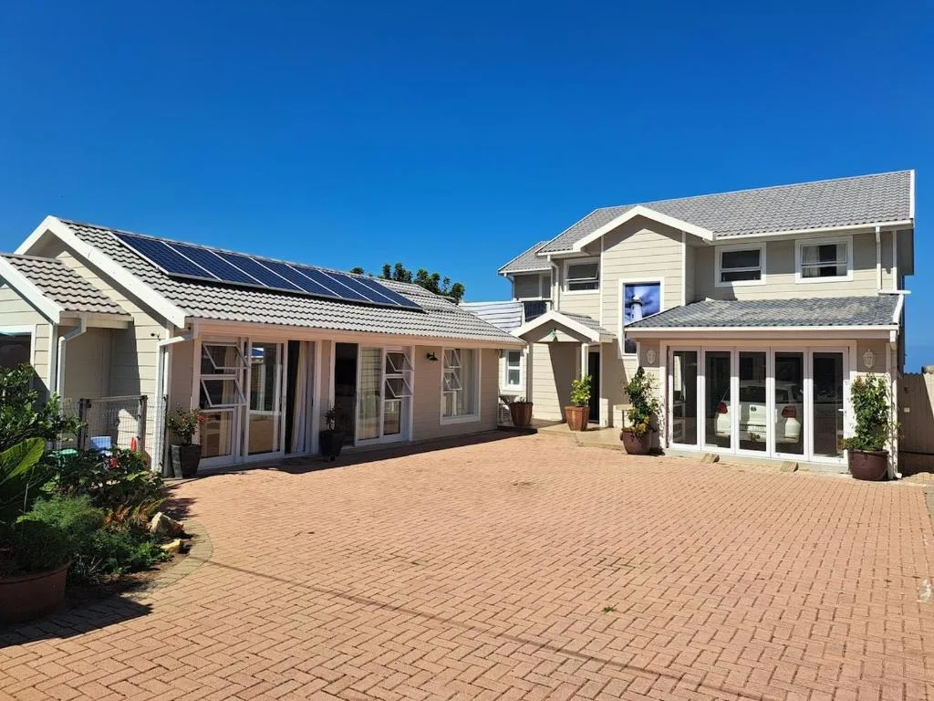 Modern two-story cottage with cream facade, solar panels, brick driveway