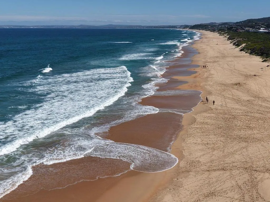 Scenic coastal beach with golden sand, rolling waves, and distant mountains