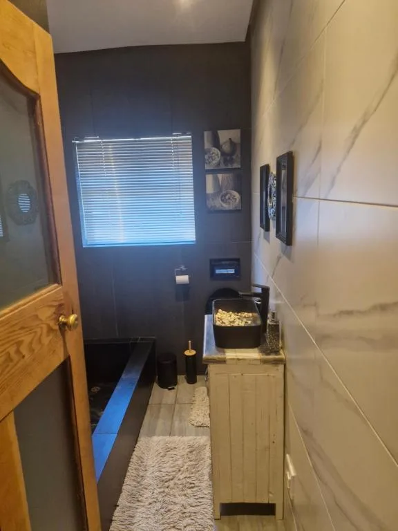 Modern bathroom with dark walls, window blinds, vanity storage, and décor.