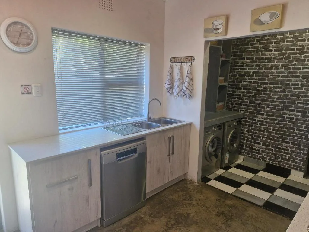 Modern kitchen with sink, dishwasher, white cabinetry, and brick feature wall
