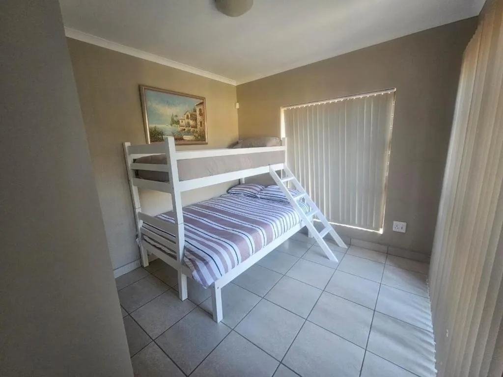 Spacious bedroom with white bunk bed and striped bedding, tile flooring