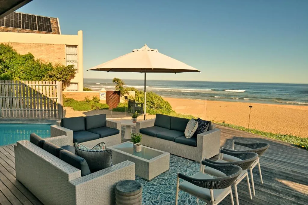 Beachfront deck with outdoor seating, umbrella, and ocean view