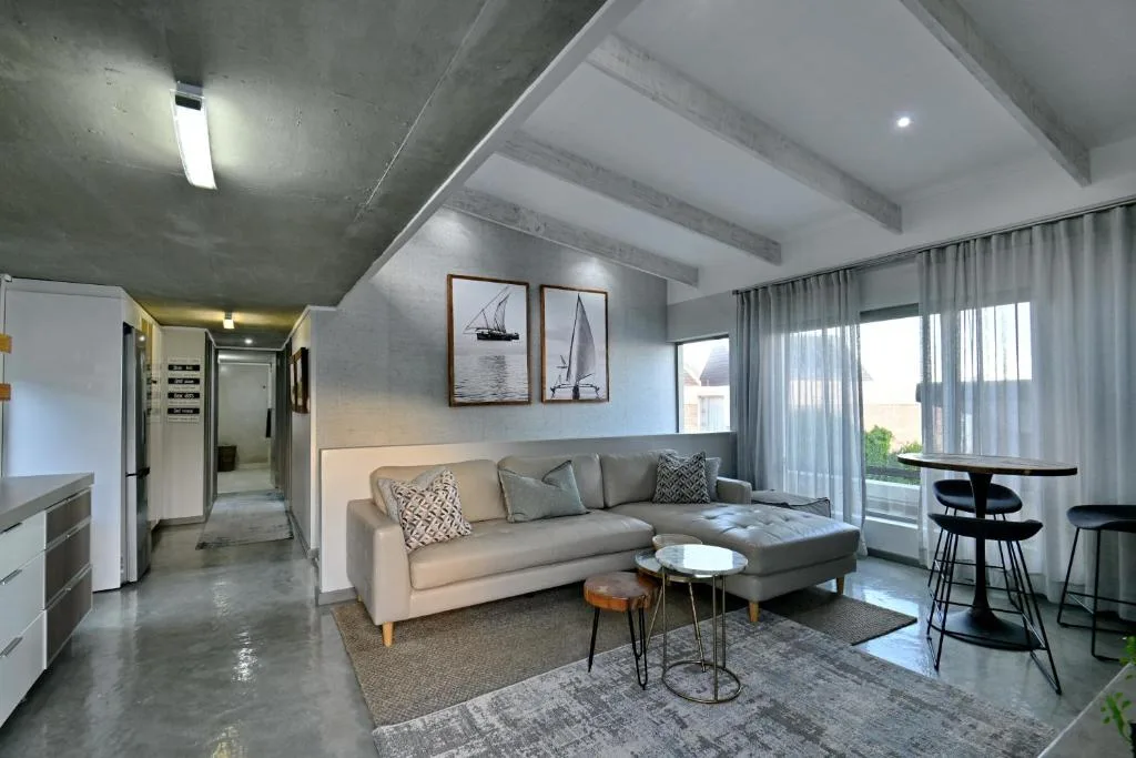 Modern open-plan lounge with beige sectional sofa, sailboat artwork, and bright windows