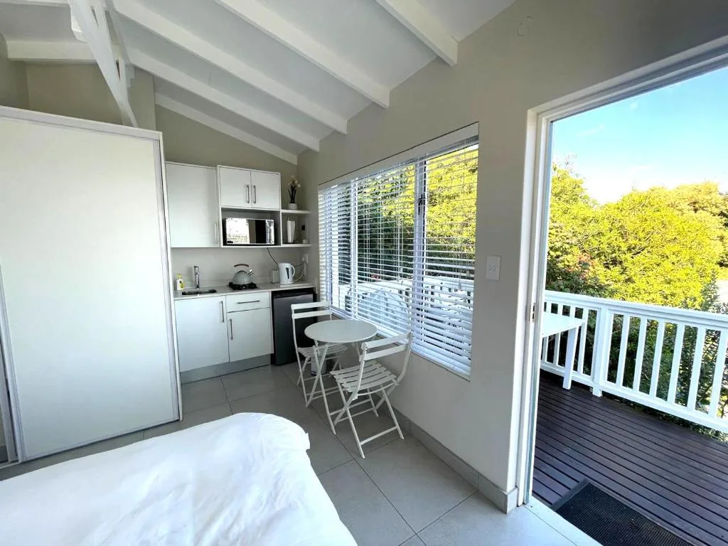 Bright bedroom with kitchenette, small dining table, and deck access overlooking trees