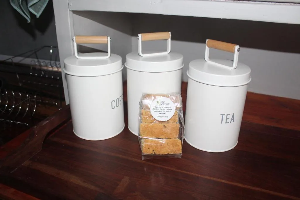 Three white ceramic storage canisters with wooden handles and packaged biscuits on wooden counter