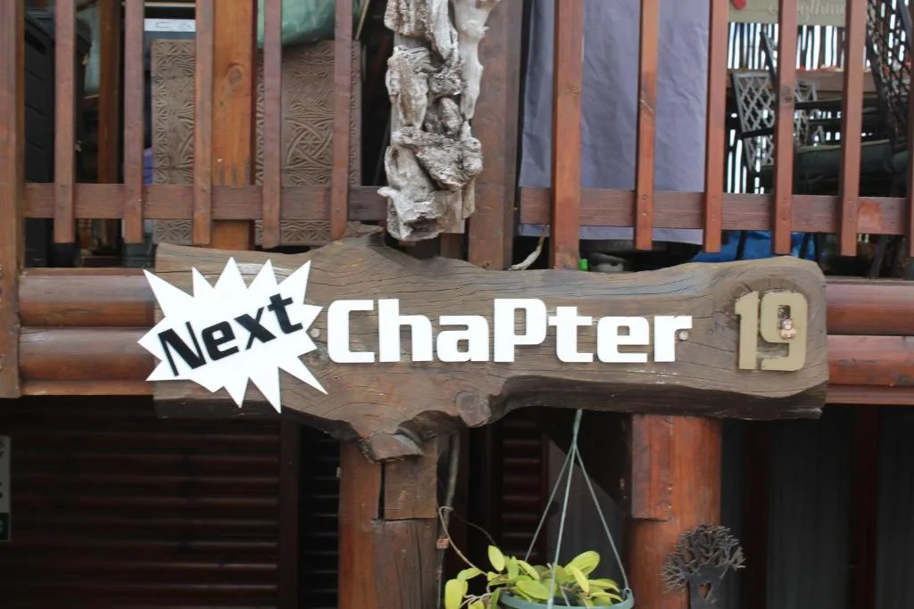Wooden signage reading Next Chapter 19 on rustic exterior wall