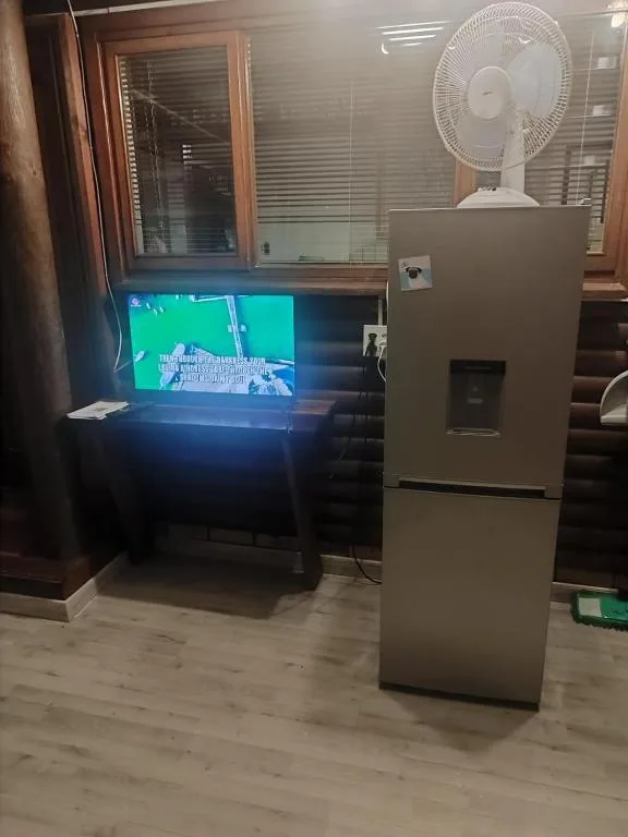 Living room with TV, refrigerator, and white fan on wooden flooring