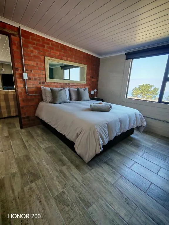 Modern bedroom with queen bed, red brick wall, and large windows overlooking garden