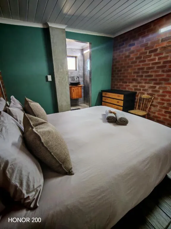 Spacious bedroom with white bed, green walls, and exposed brick feature