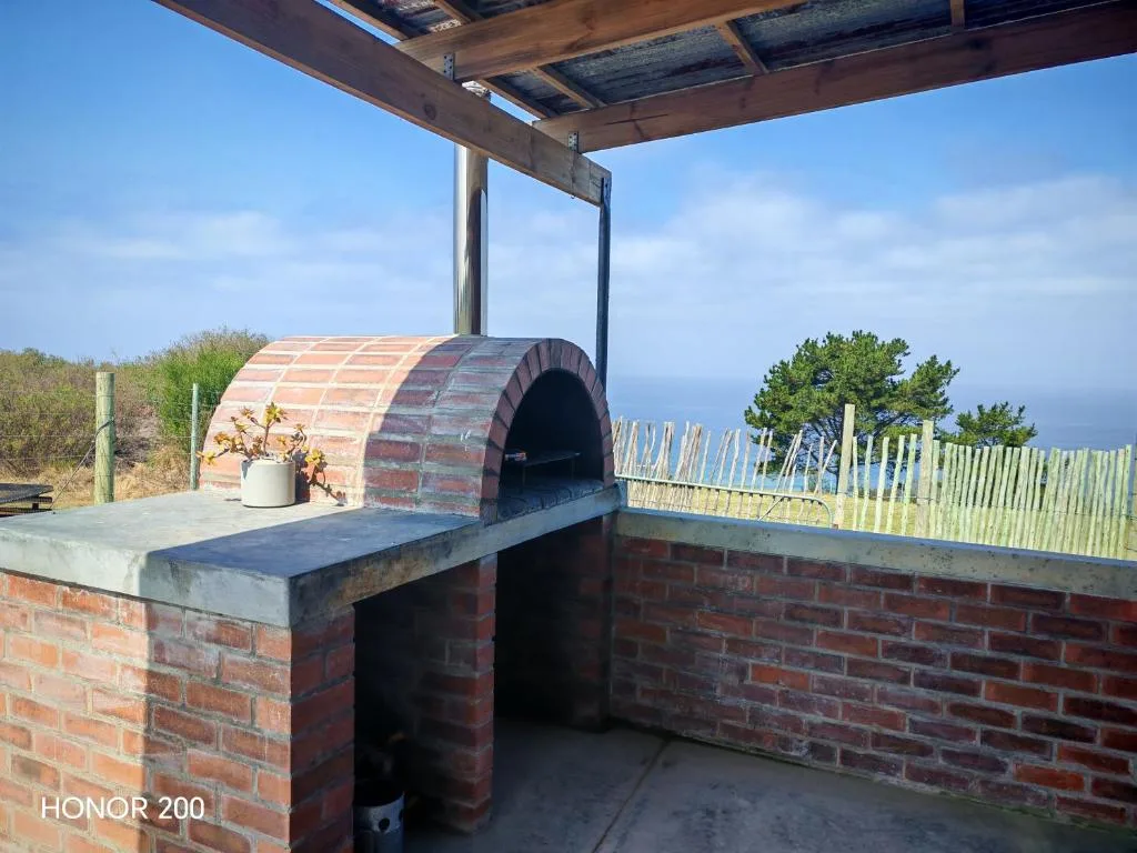Brick pizza oven under pergola with ocean view and white fence