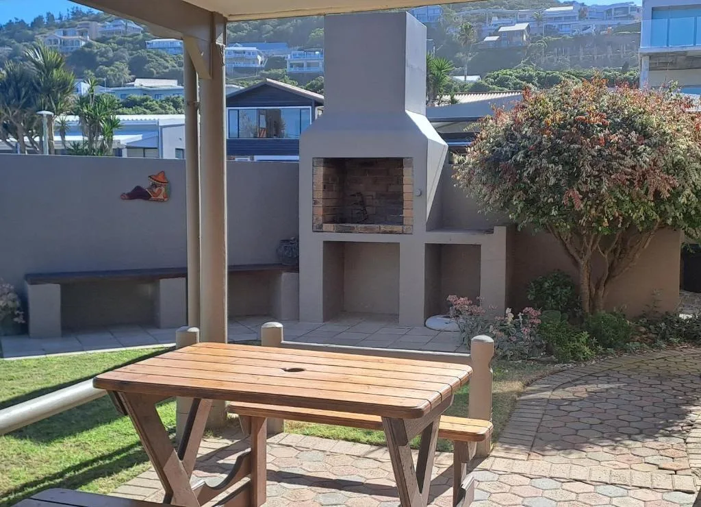 Wooden picnic table on paved deck with garden and braai area view