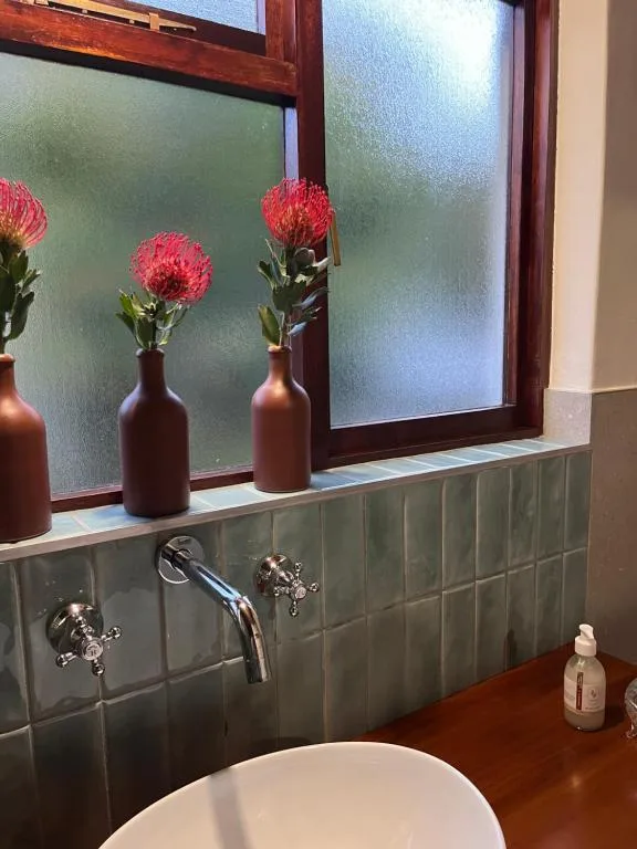 Bathroom vanity with red protea flowers in bronze vases and tiled backsplash