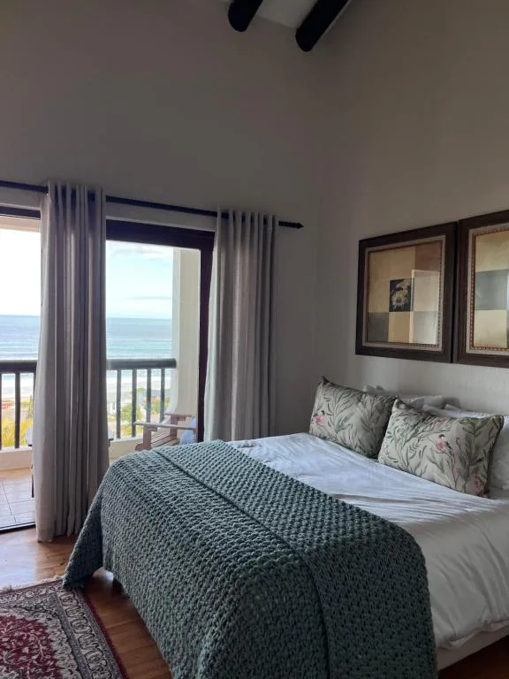 Bedroom with ocean view through glass doors and coastal scenery beyond