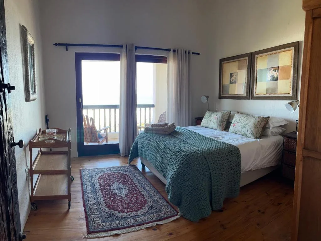 Bright bedroom with queen bed, blue doors opening to balcony, coastal views