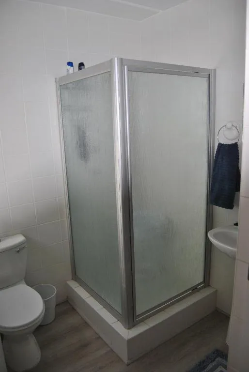 Clean bathroom with corner shower enclosure, toilet, and white tiled walls