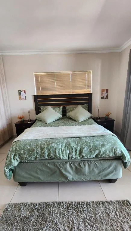 Bedroom with queen bed, green bedding, dark headboard, and side tables