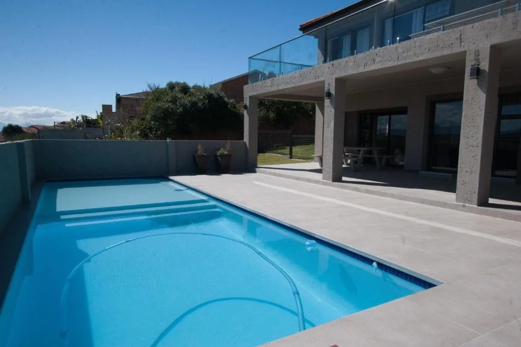 Bright blue swimming pool with modern house and deck area overlooking gardens