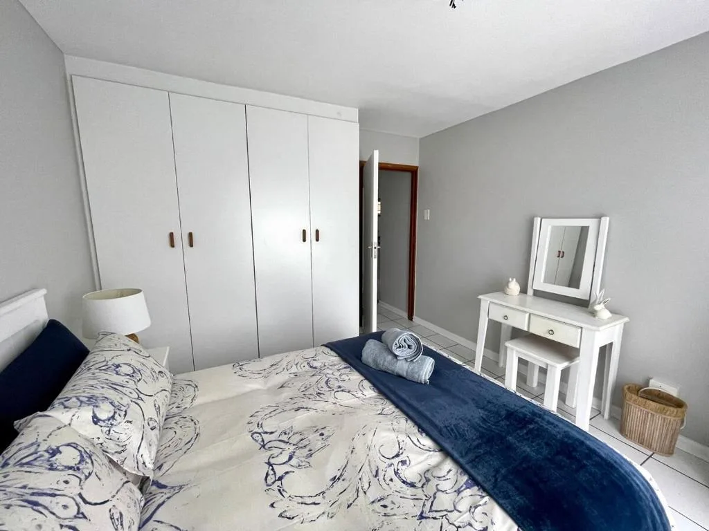 Bright bedroom with queen bed, white wardrobe, and vanity mirror setup