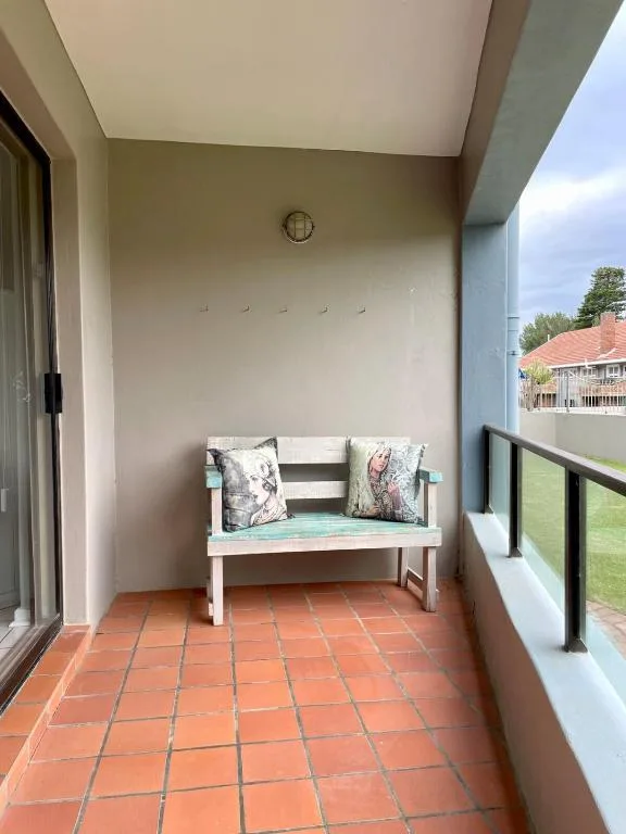 Covered balcony with white bench and colorful cushions overlooking garden