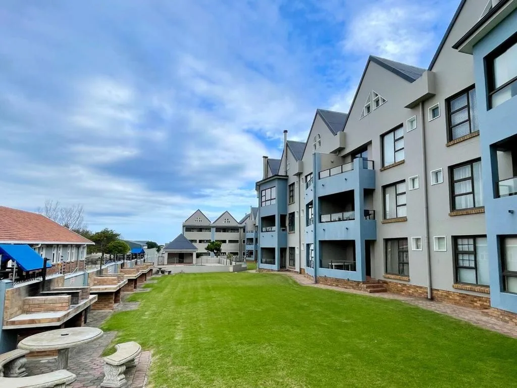 Modern waterfront apartment complex with manicured lawn and coastal setting.