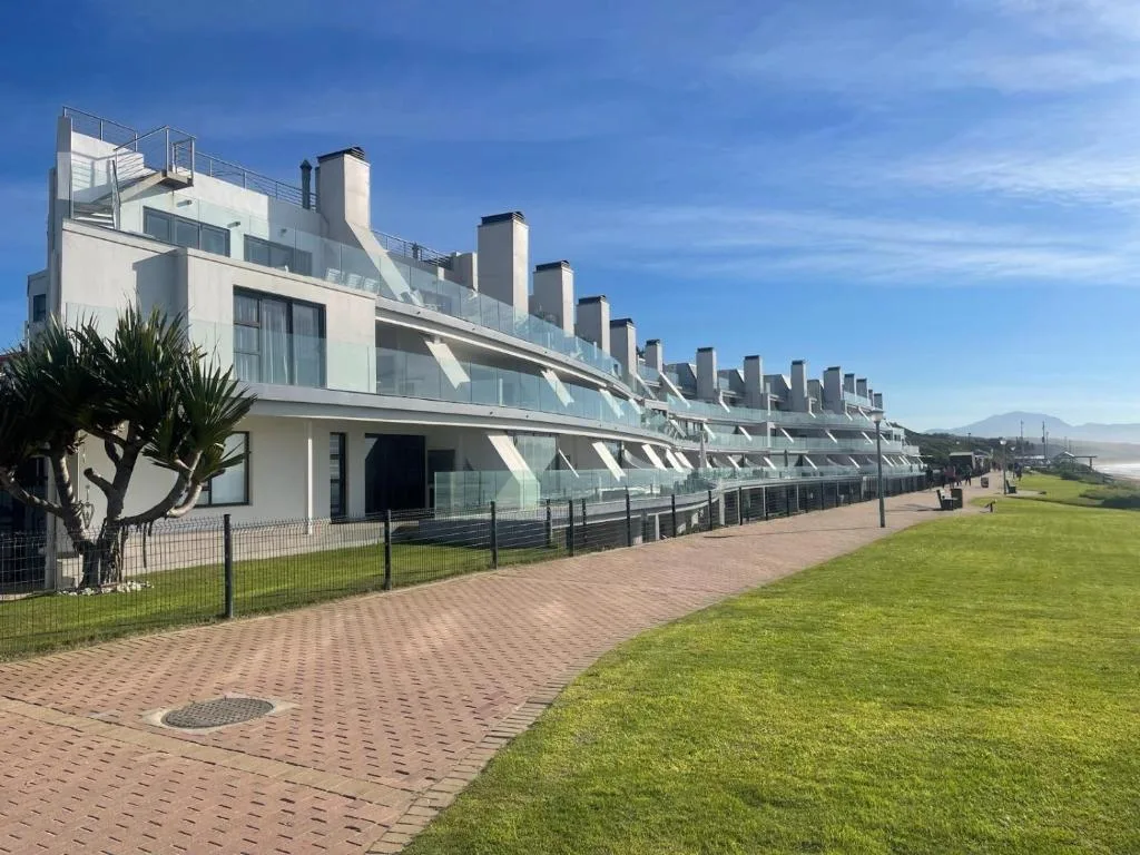 Modern white apartment building with multiple units and rooftop terraces along manicured gardens