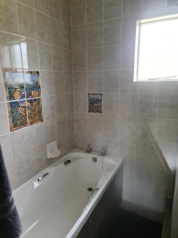 Tiled bathroom with white bathtub, shower enclosure, and window
