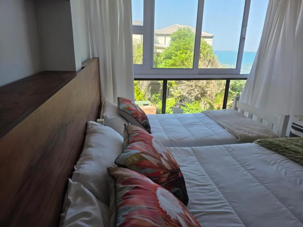 Bedroom with ocean view through large windows overlooking coastal landscape
