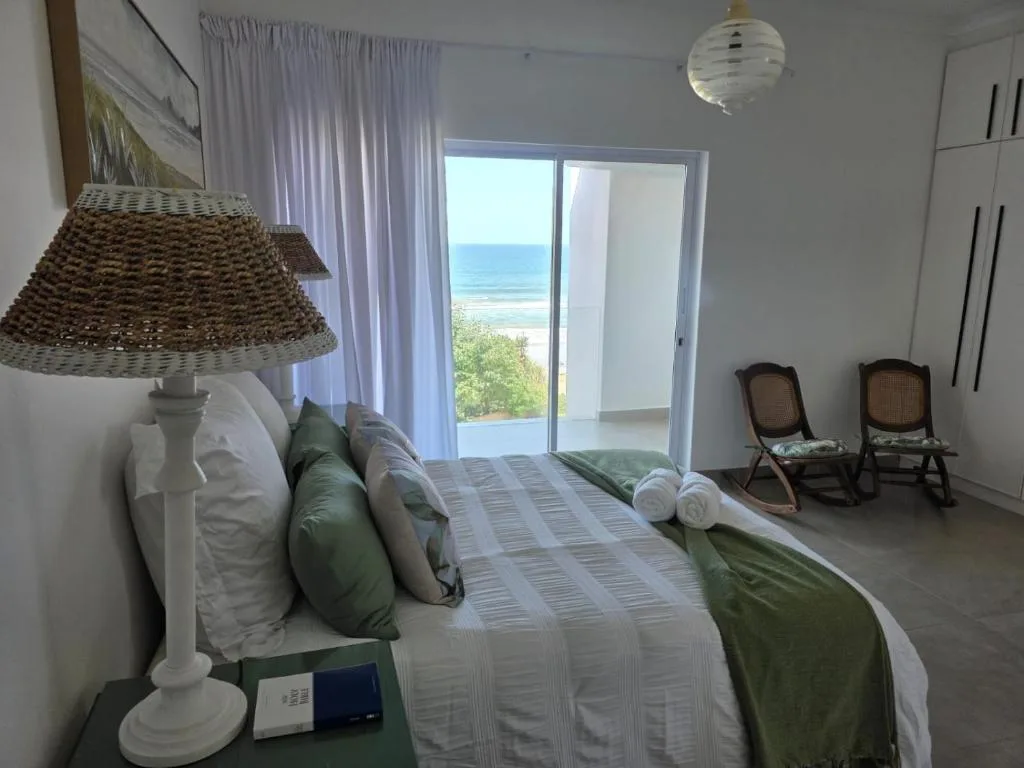 Bright bedroom with ocean view through glass doors and coastal landscape beyond