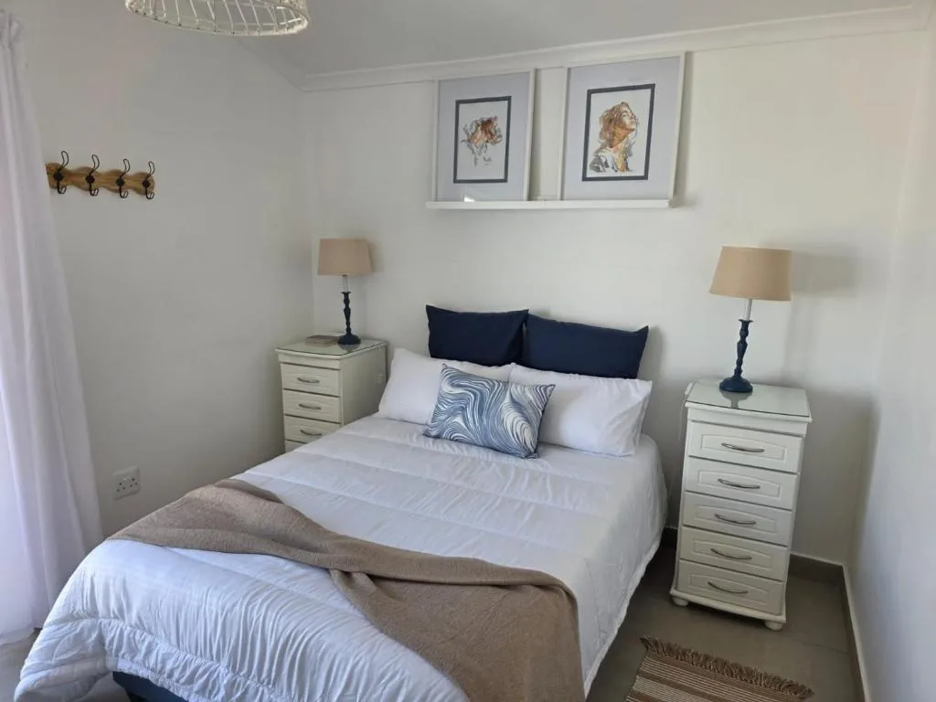 Bright bedroom with queen bed, white linens, dark blue pillows, matching bedside tables